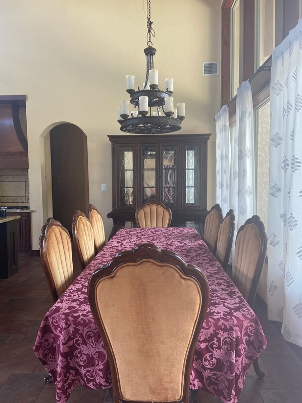 Een eetkamer met een lange tafel, zes stoelen, een kroonluchter en een kast met glazen deuren.