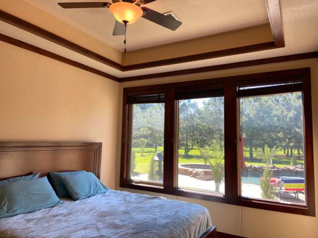 Une chambre à coucher avec un lit, un ventilateur de plafond et de grandes fenêtres donnant sur un parc.