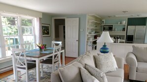 A living room with a sofa, a dining table with chairs, a kitchen area with a microwave, and a door leading to another room. - Charming Kennebunkport overlooking the Cape Arundel Golf Course (Kennebunkport)