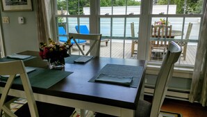 A dining area with a table set for two, a vase of flowers, and a view of the pool and deck chairs outside. - Charming Kennebunkport overlooking the Cape Arundel Golf Course (Kennebunkport)