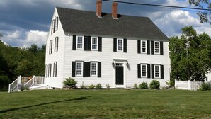 A two-story white house with black shutters, a brick chimney, and a white picket fence. - Charming Kennebunkport overlooking the Cape Arundel Golf Course (Kennebunkport)