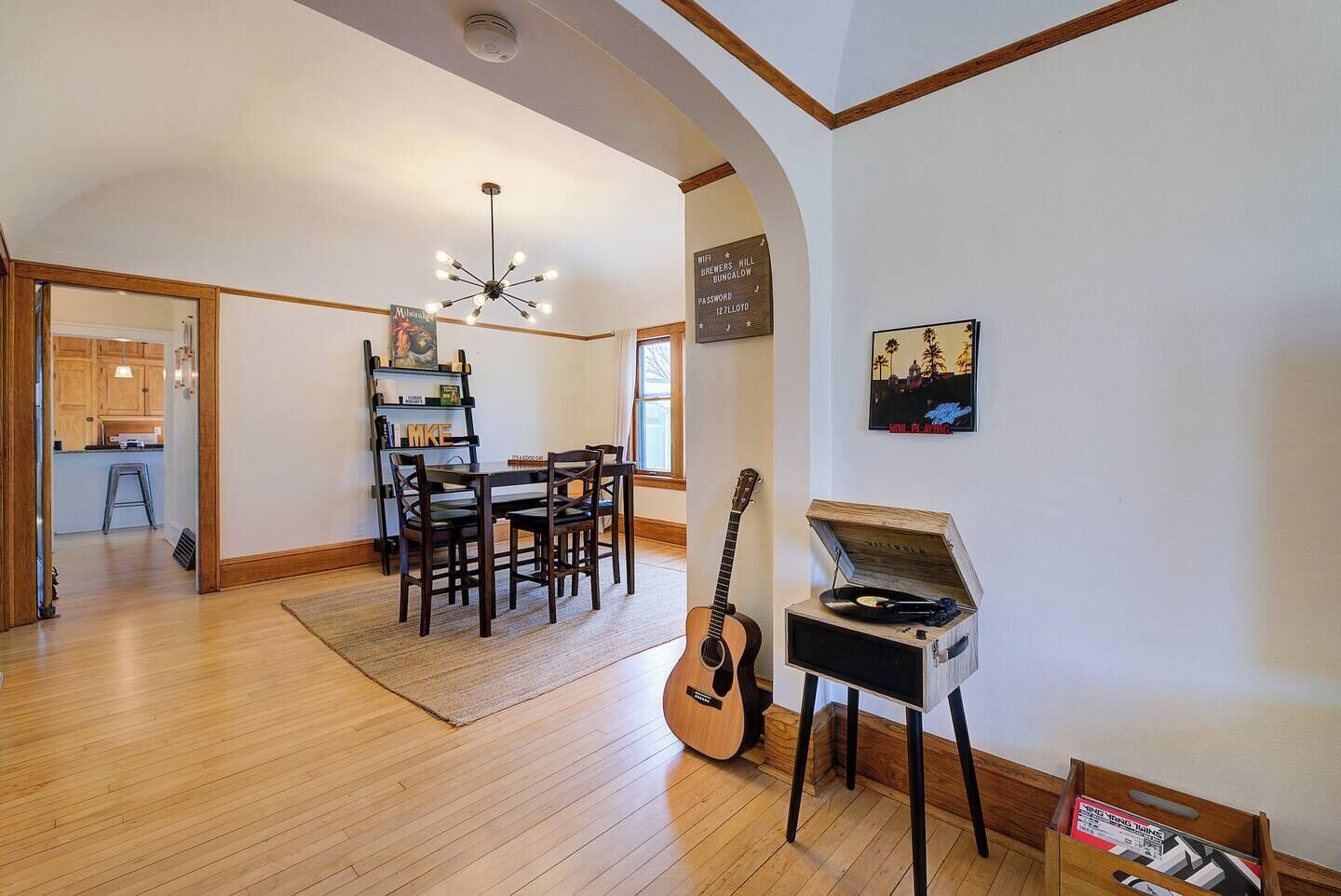 A spacious living room with a wooden floor, a dining area with a table and chairs, a guitar, and a record player.