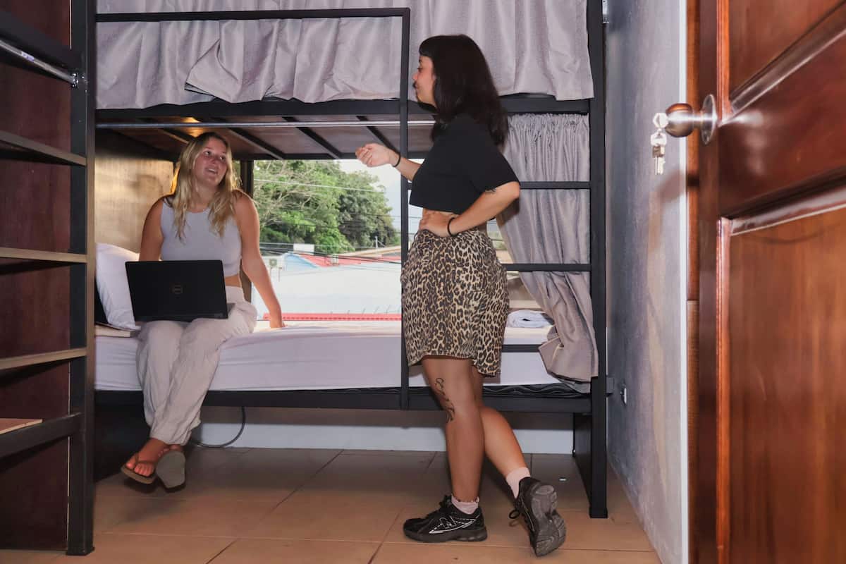 A bunk bed room with a laptop on the lower bunk and a person standing on the upper bunk.