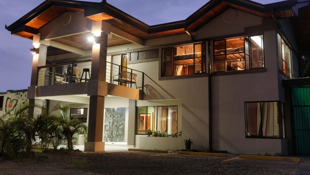 A modern two-story house with a balcony, large windows, and a well-lit interior. - Ceiba Eco Hostel (La Fortuna)