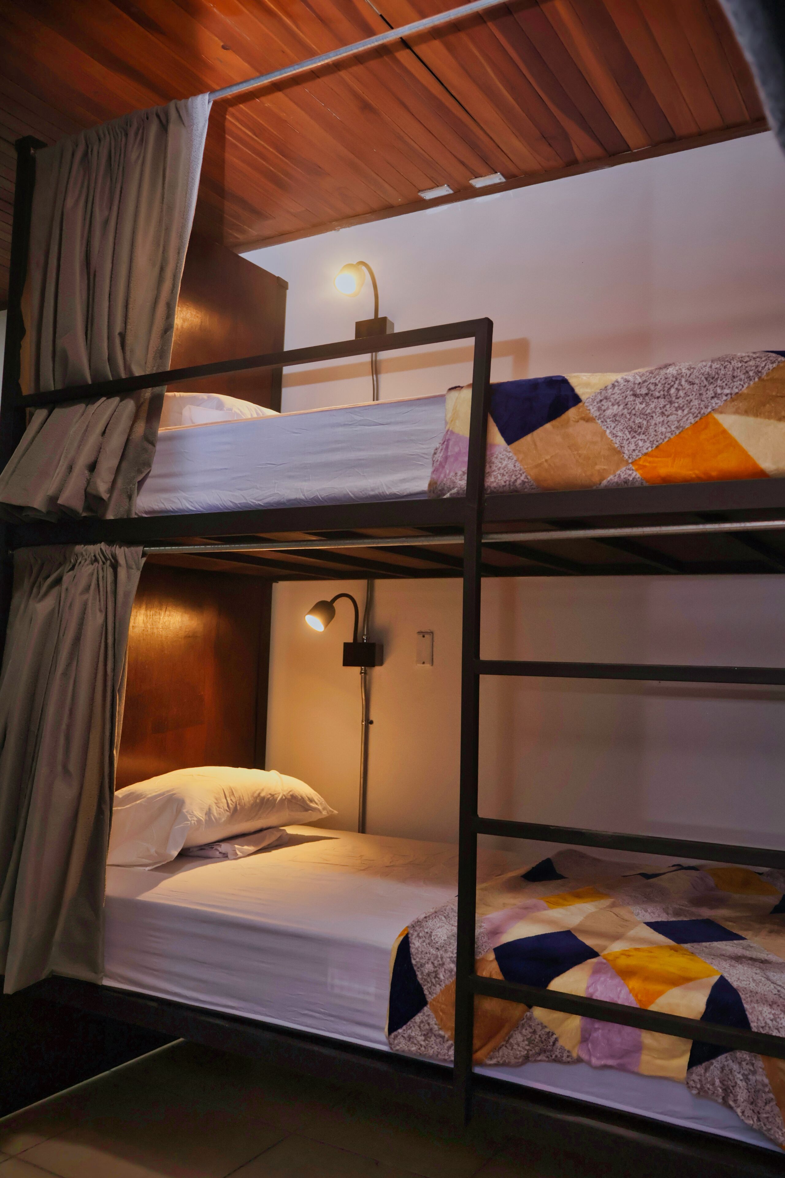 A bunk bed room with a wooden ceiling, a bedside lamp, and a quilted blanket.