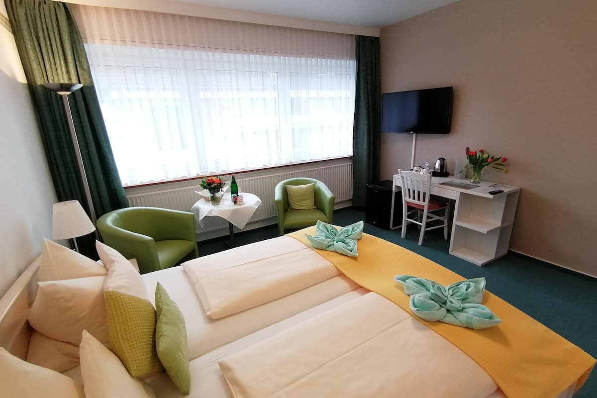 Une chambre d’hôtel avec un lit, deux chaises, un bureau, une télévision et une fenêtre avec des rideaux.