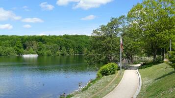 A lakeside path with a boat dock, lush greenery, and a clear sky.