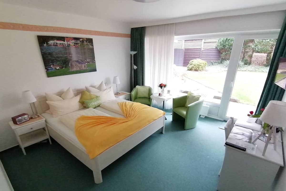 Une chambre d’hôtel avec un lit, une table de chevet, une lampe, un fauteuil vert et un bureau avec une chaise.