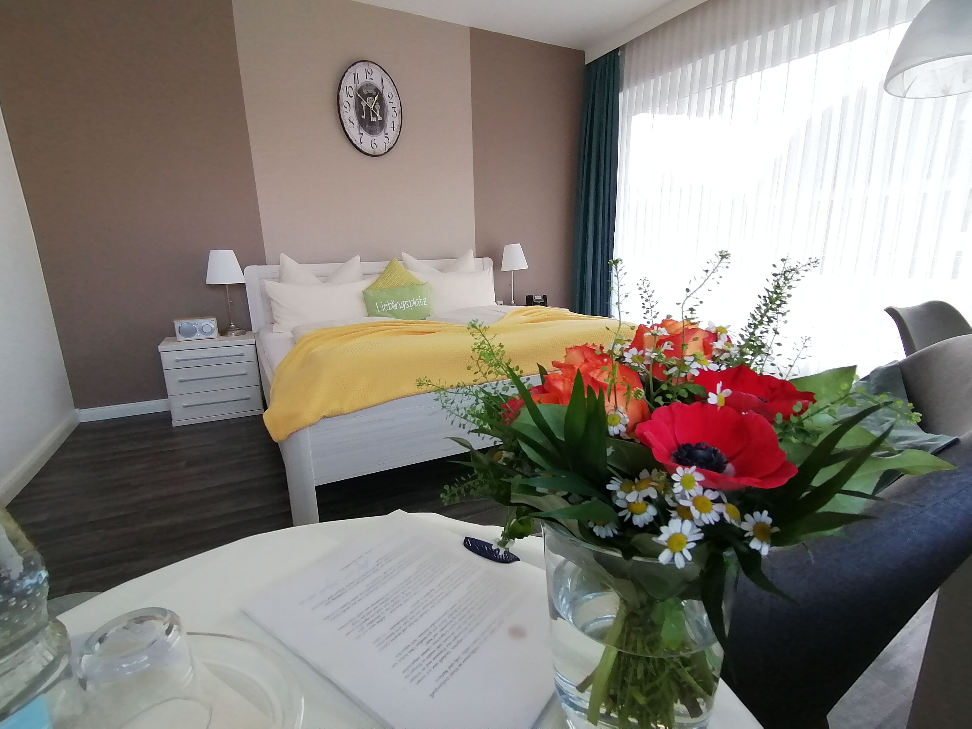 Een hotelkamer met een bed, nachtkastje, lamp en een bloemenarrangement op de tafel.