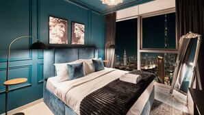 Camera da letto con vista sulla città, un letto con numerosi cuscini, una lampada da terra e un grande specchio.