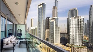 Un balcon offrant une vue sur la ville, notamment sur le Burj Khalifa et les bâtiments modernes, ainsi qu’un espace détente avec des coussins et un fauteuil suspendu.