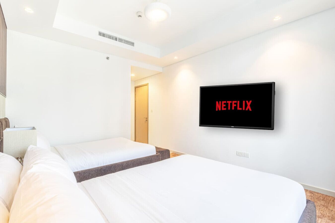Habitación de hotel con dos camas, un televisor mostrando el logotipo de Netflix y una puerta que da a otra habitación.
