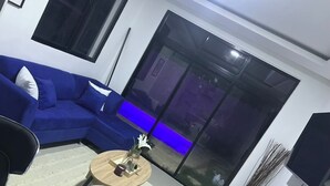 A modern living room with a blue sofa, black chairs, a round wooden coffee table, and a large window with a view of a garden. - Elegant 2-bedroom villa oasis in Punta Cana with WiFi and AC (Punta Cana)
