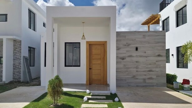 A modern two-story house with a clean, minimalist design, featuring a wooden front door, a small garden with stepping stones, and a stone wall. - Elegant 2-bedroom villa oasis in Punta Cana with WiFi and AC (Punta Cana)