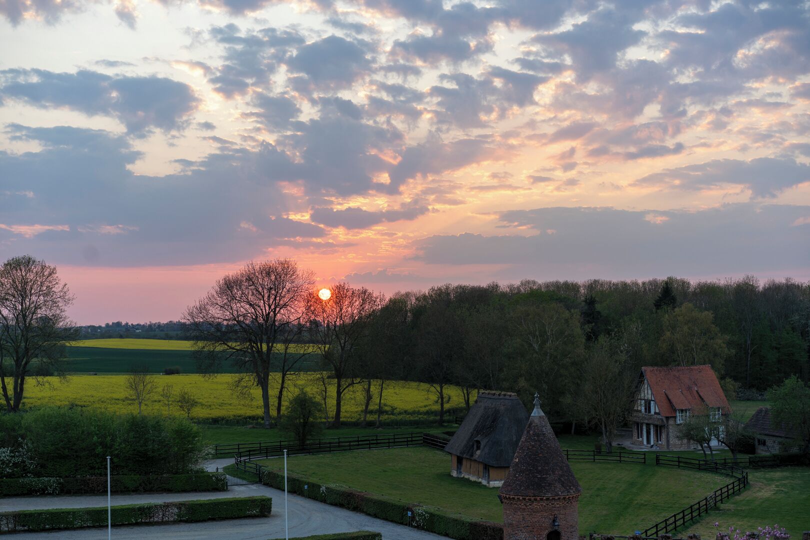 A rural landscape with a sunset, a thatched-roof house, and a brick tower.