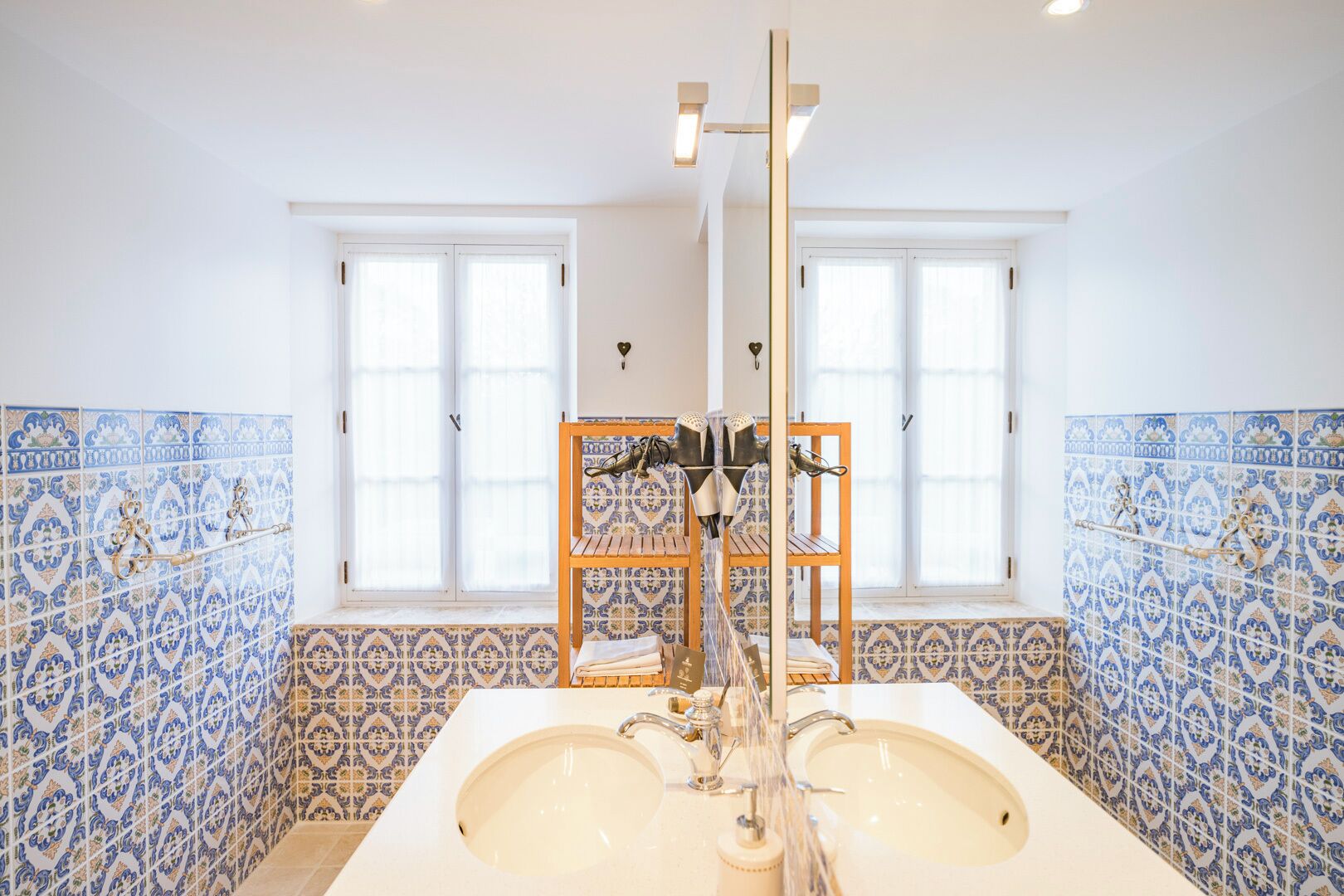 A bathroom with two sinks, a mirror, and a shelf with toiletries.