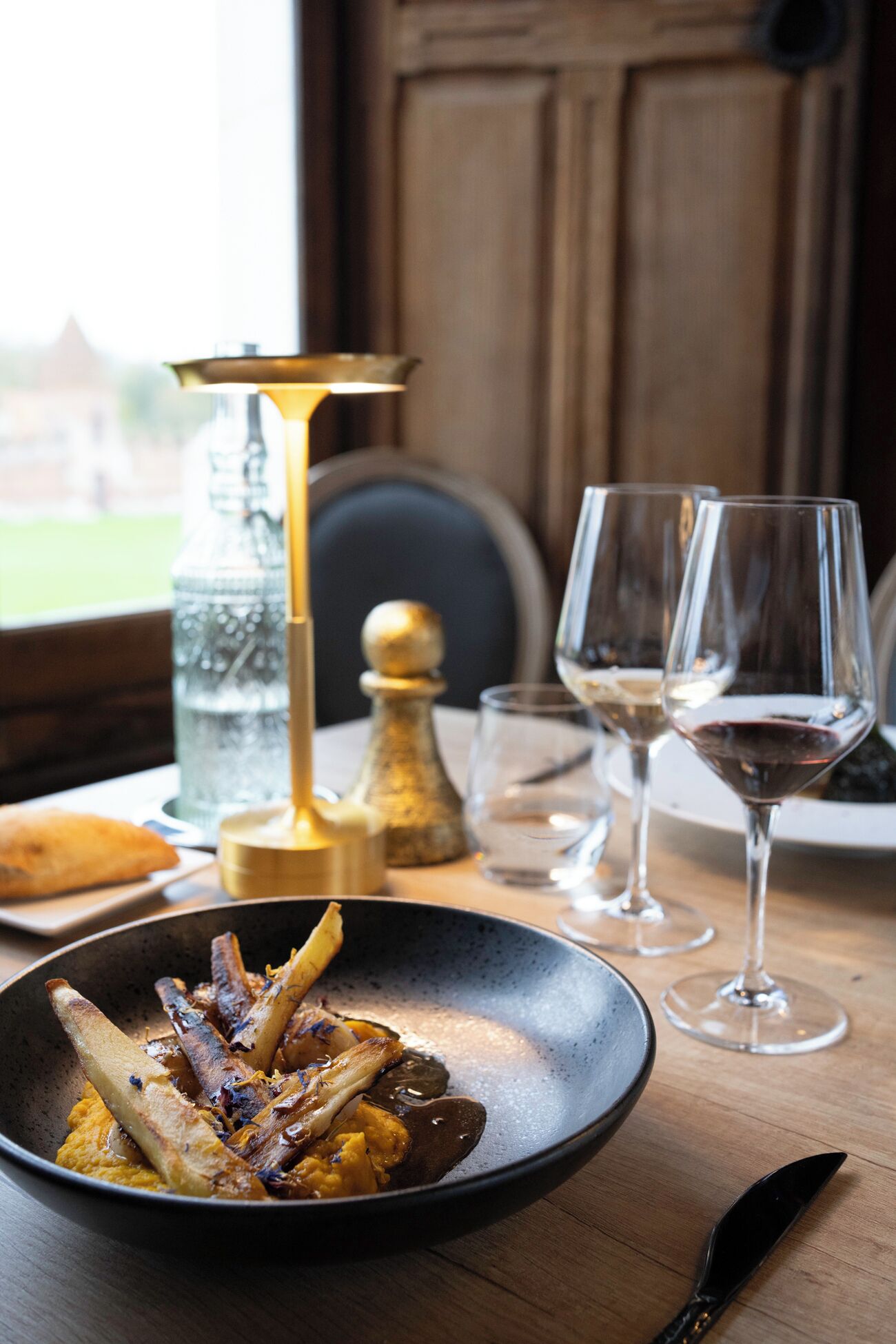 Een eettafel met een bord eten, twee wijnglazen, een waterfles en een zout- en peperstel.
