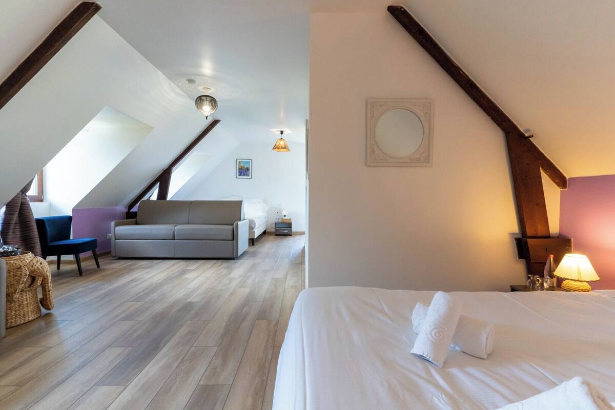 Camera da letto moderna mansardata con tetto spiovente, un letto grande, una poltrona e un tavolo da pranzo.