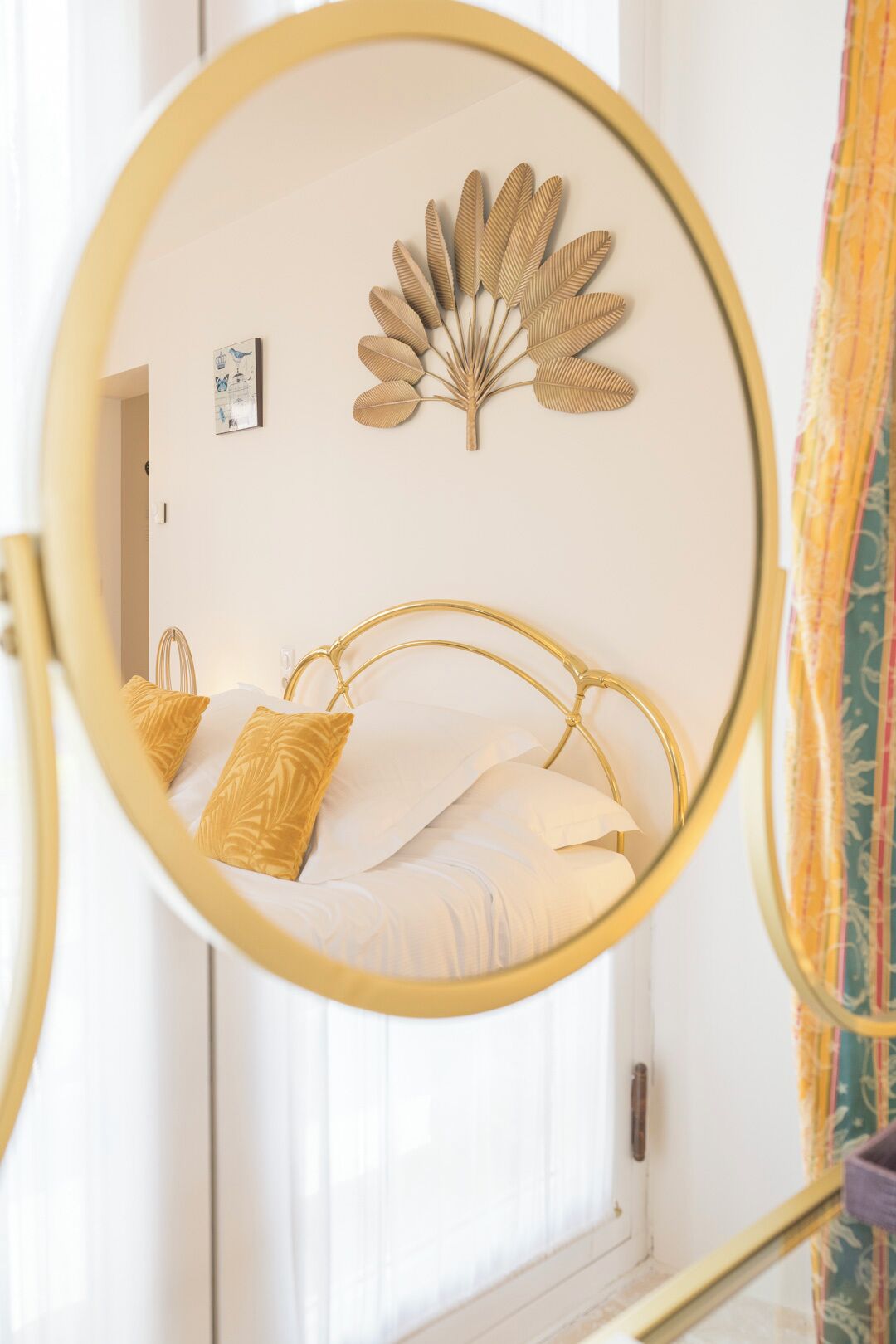 A bed with a gold frame, white bedding, and a decorative leaf wall art piece.