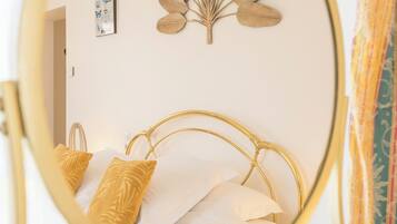 A bed with a gold frame, white bedding, and a decorative leaf wall art piece.