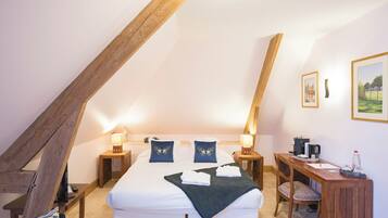 Een slaapkamer met een schuine plafond, een bed met witte lakens, twee nachtkastjes met lampen, een houten bureau en een stoel.