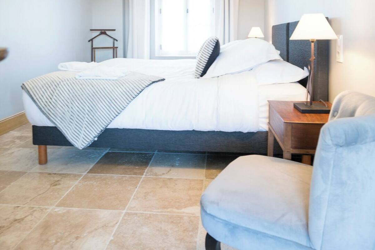 Una camera da letto con un letto, una sedia, una scrivania, una lampada, una finestra con tende e un lampadario.