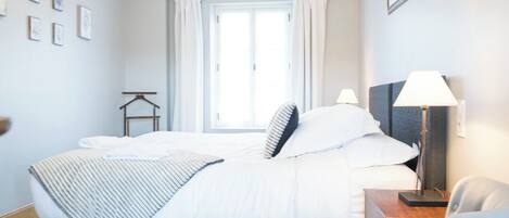Ein Schlafzimmer mit Bett, Stuhl, Schreibtisch, Lampe, einem Fenster mit Vorhängen und einer Kristallleuchter.