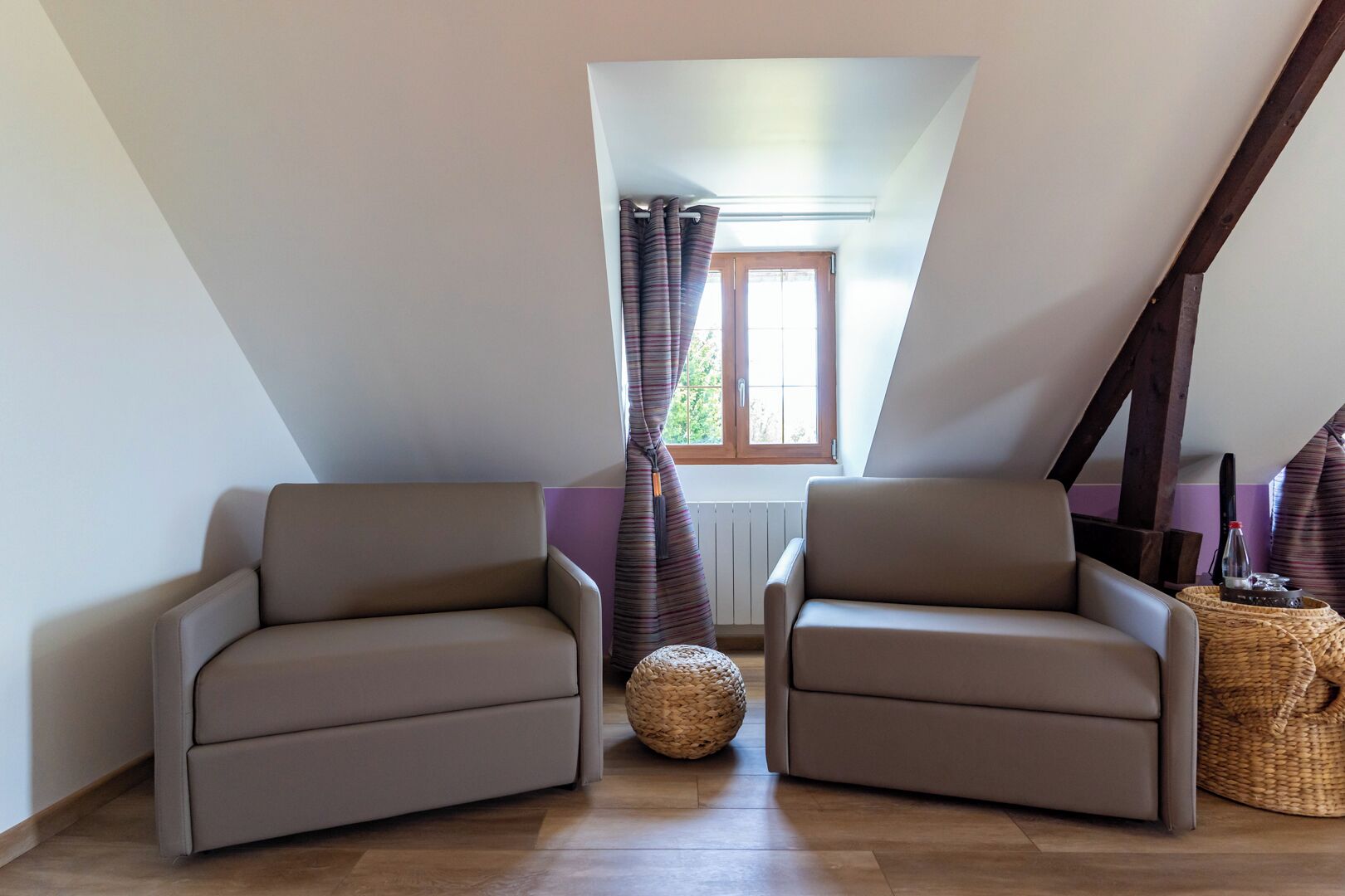 A room with two armchairs, a woven basket, a window with curtains, and a radiator.