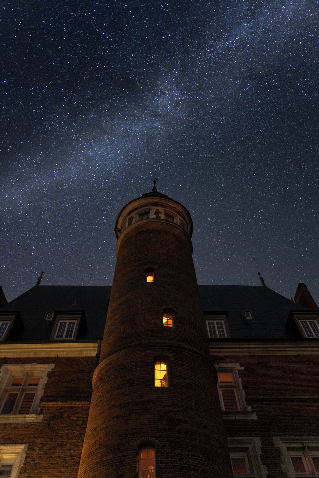 Una torre de ladrillo con múltiples ventanas, sobre un cielo nocturno estrellado.