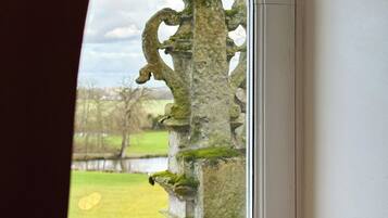 A window with a view of a stone structure with moss, a grassy field, and a cloudy sky.