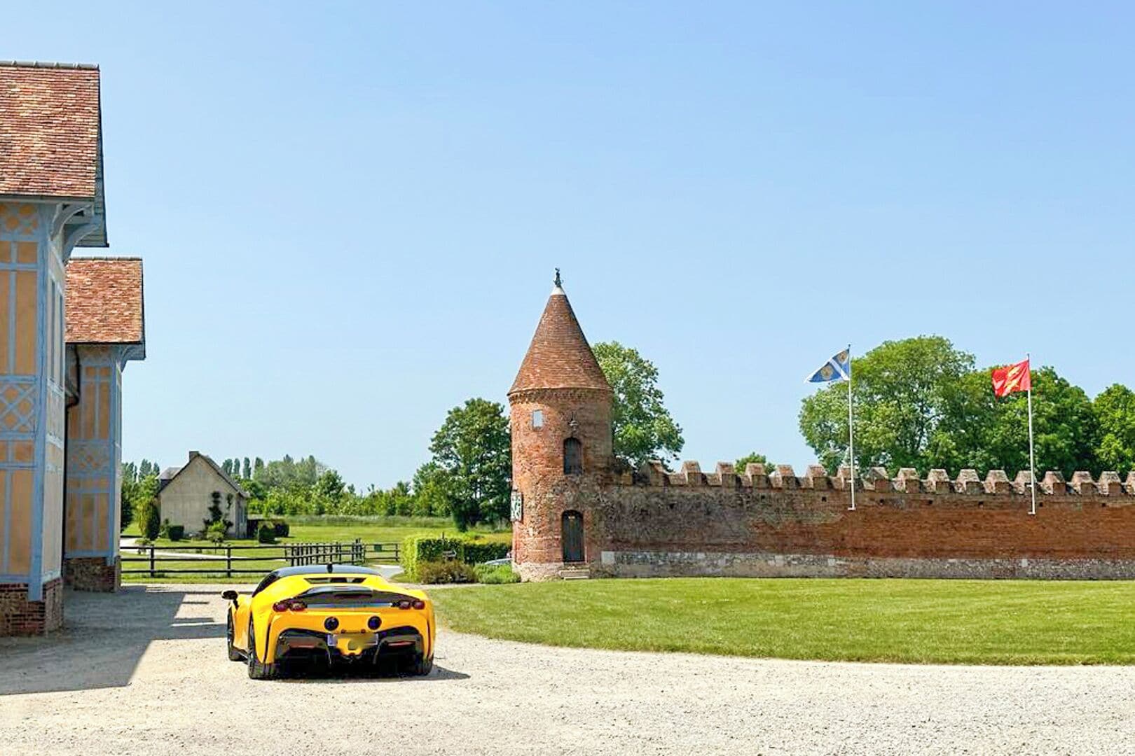 A yellow sports car parked in front of a historic building with a tower, surrounded by a grassy area and a stone wall.