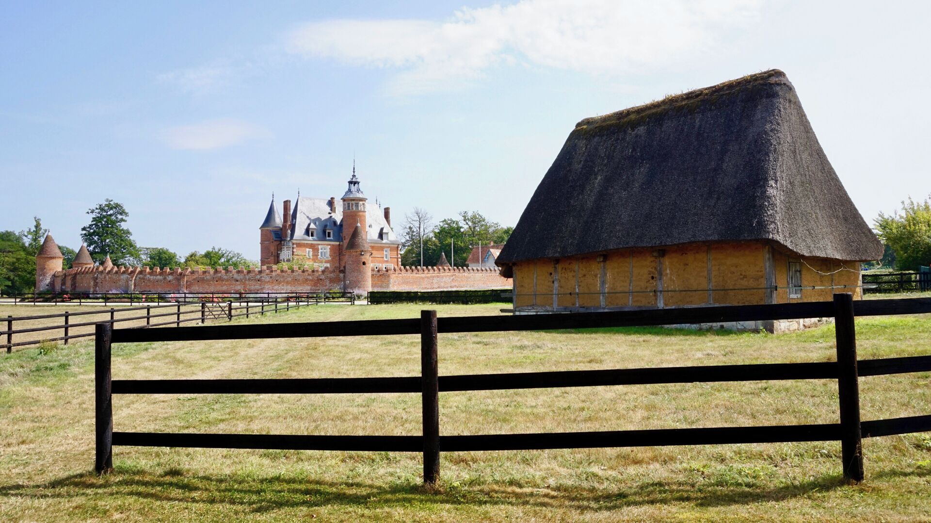 A historic building with a thatched-roof structure and a brick fortification.