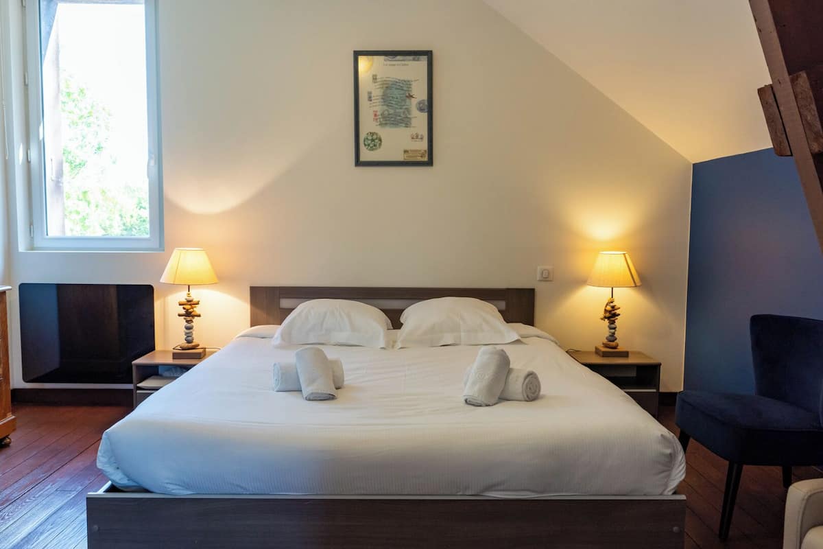Un letto rifatto con lenzuola e asciugamani bianchi, due abat-jour, un certificato incorniciato appeso al muro e una finestra con vista su del verde.