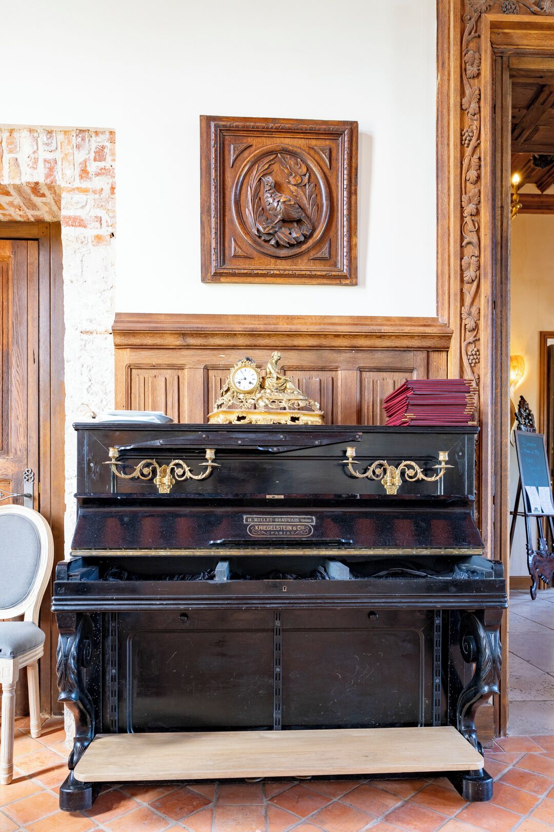 Un piano de cola en una habitación con pared de ladrillo, una obra de arte enmarcada y una puerta de madera.