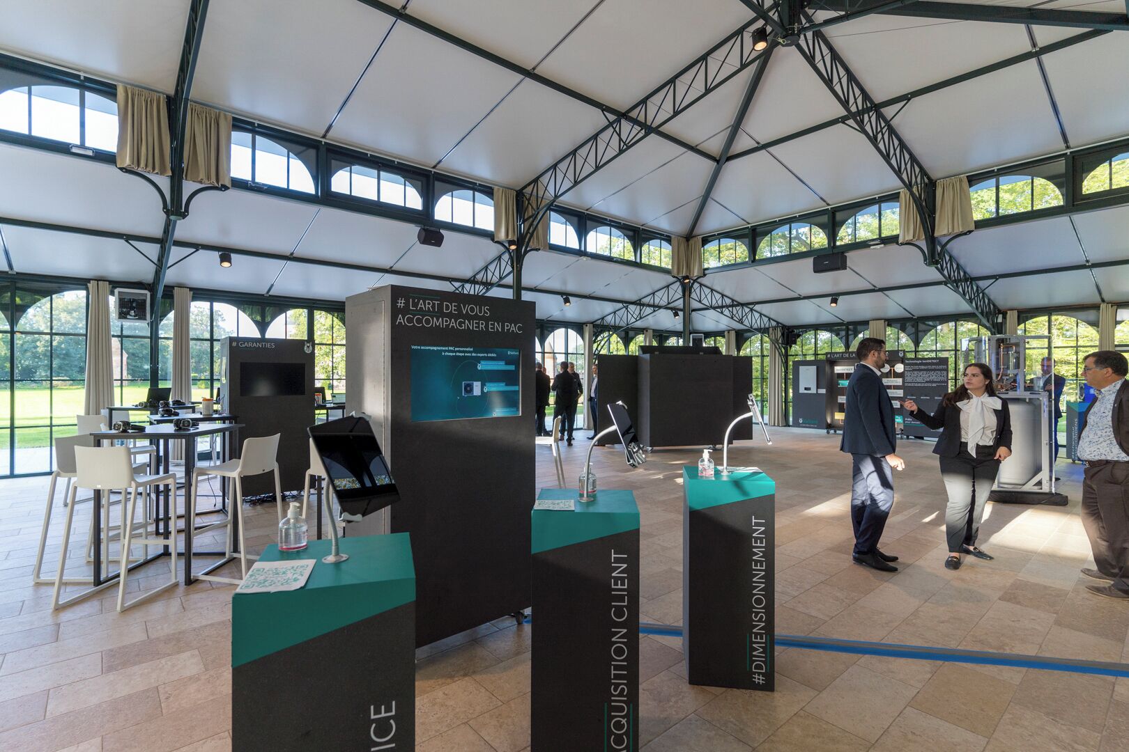 Ruime binnenruimte met hoge plafonds en grote ramen, met tafels en stoelen en een balie met presentatie.