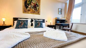 Een hotelkamer met een groot bed, twee bedlampen, een bureau en een raam met gordijnen.