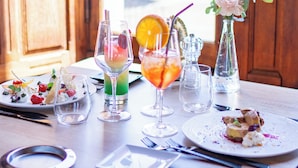 Une table à manger dressée avec différents plats et boissons, un vase rempli de fleurs et une vue sur la verdure à l’extérieur.