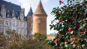 Un bâtiment historique doté d’une tour imposante et d’un jardin agrémenté de fleurs rouges.
