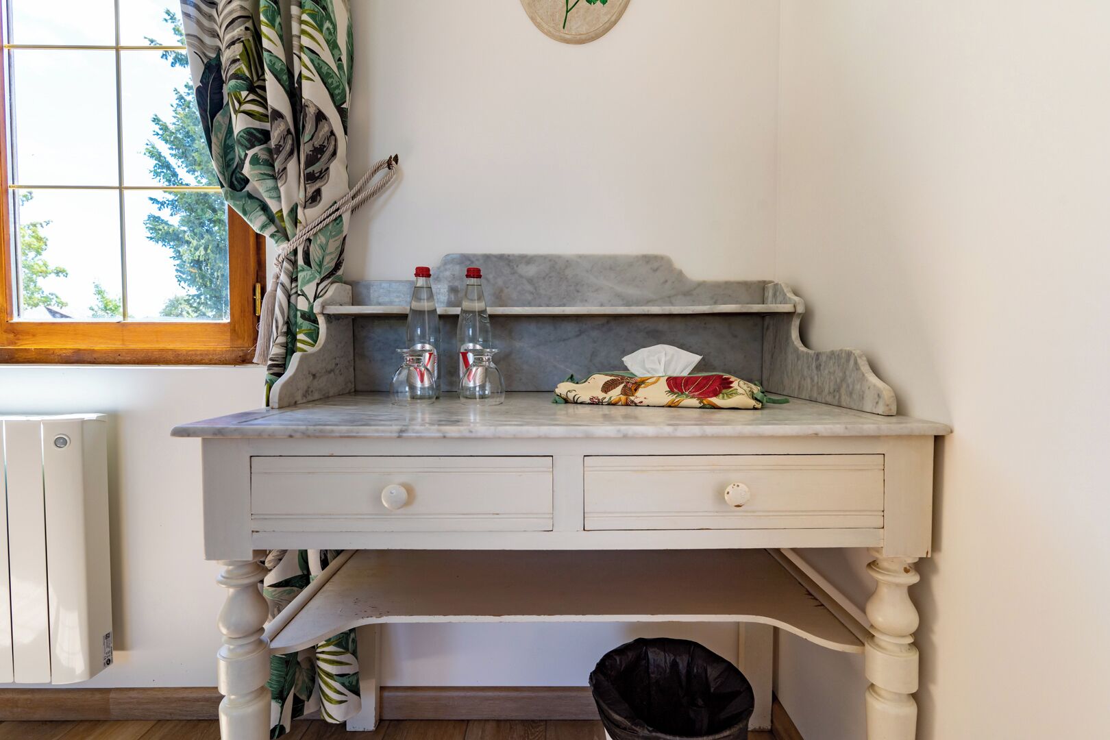 A small, white wooden desk with two bottles of water, a tissue, and a decorative pillow.