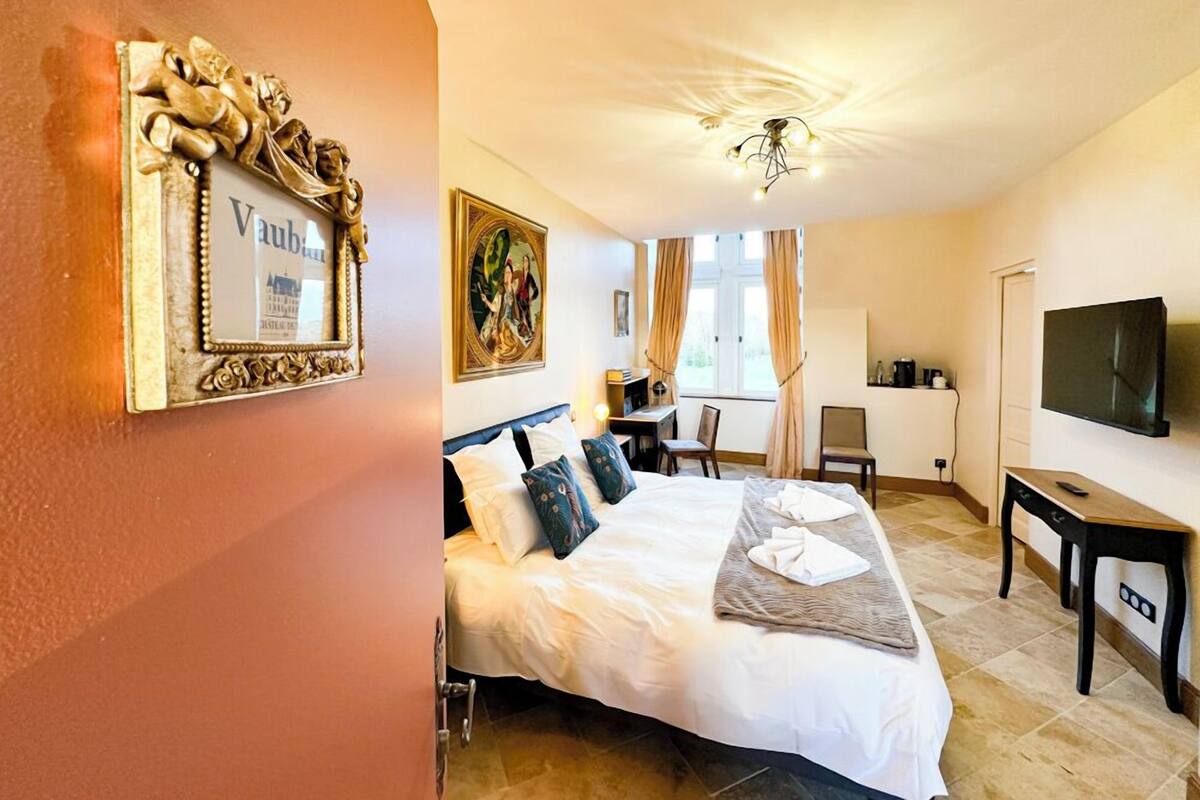 Camera d'albergo con un letto grande, una scrivania, una sedia, una televisione e una finestra con tende.