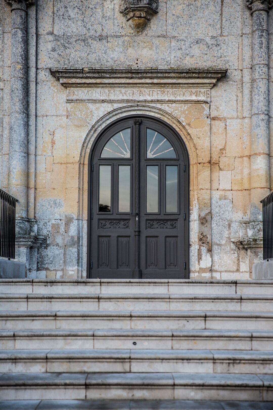 A large, dark wooden door with a decorative arch above it, set in a stone building with steps leading up to the entrance.