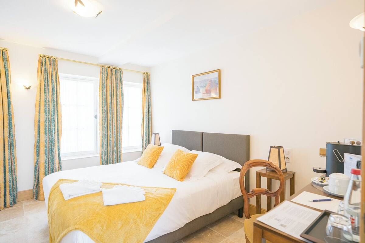 Una camera d'albergo con un letto, tende, una scrivania con una sedia e un quadro appeso al muro.