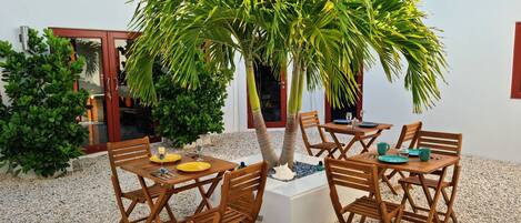 A patio with a wooden table and chairs, surrounded by a small palm tree and other greenery.