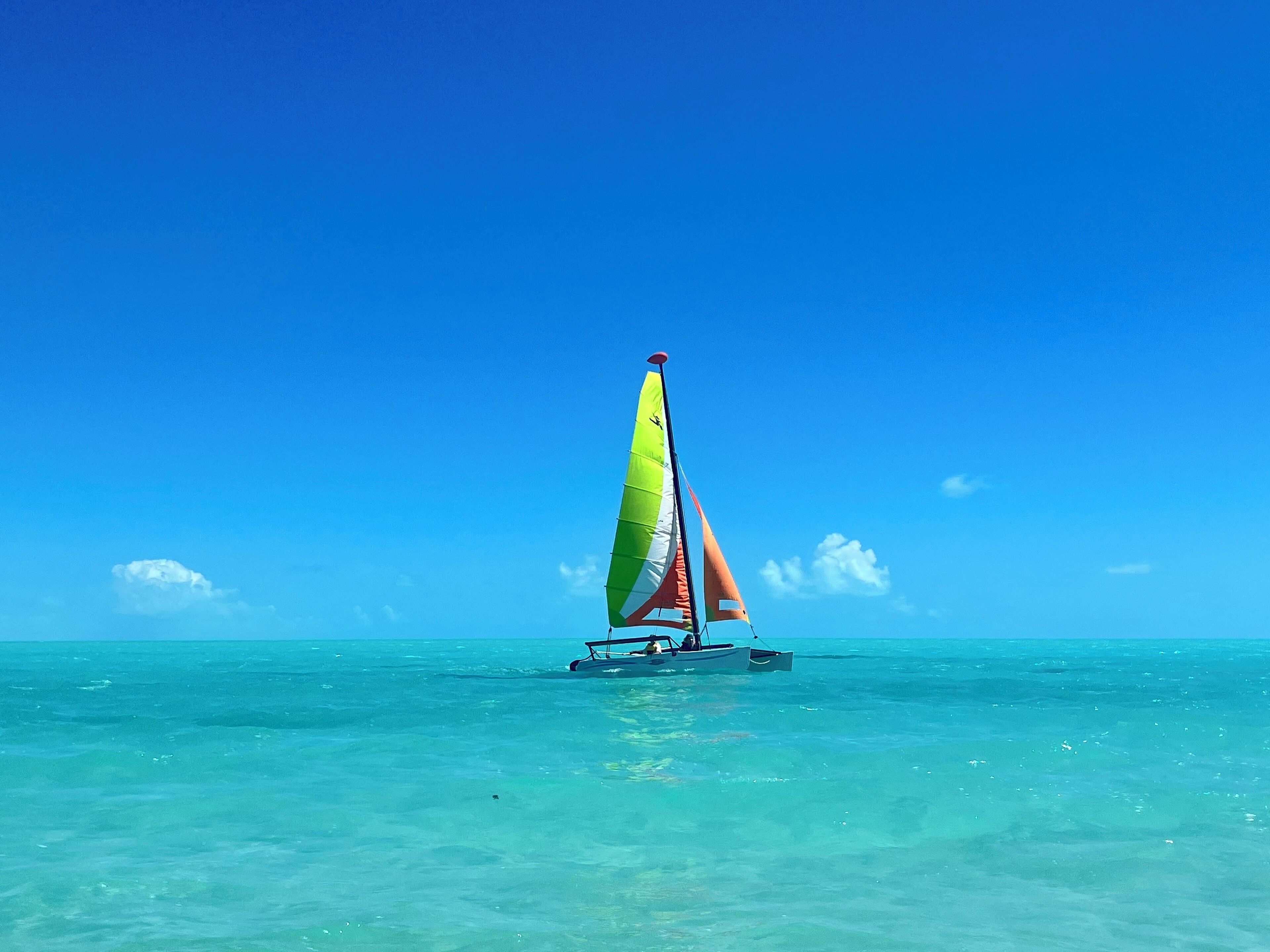 Un velero con una vela colorida sobre aguas turquesas cristalinas bajo un cielo azul.