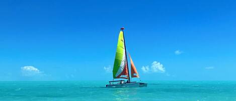 Un velero con una vela colorida sobre aguas turquesas cristalinas bajo un cielo azul.