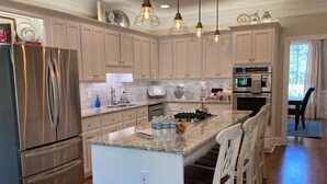 A modern kitchen with stainless steel appliances, a central island with bar stools, pendant lighting, and a view of the dining area. - Masters Tournament Rental; 4 Bed, 2.5 Bath-4 Bedroom Home in Heart of Evans, GA (Evans)