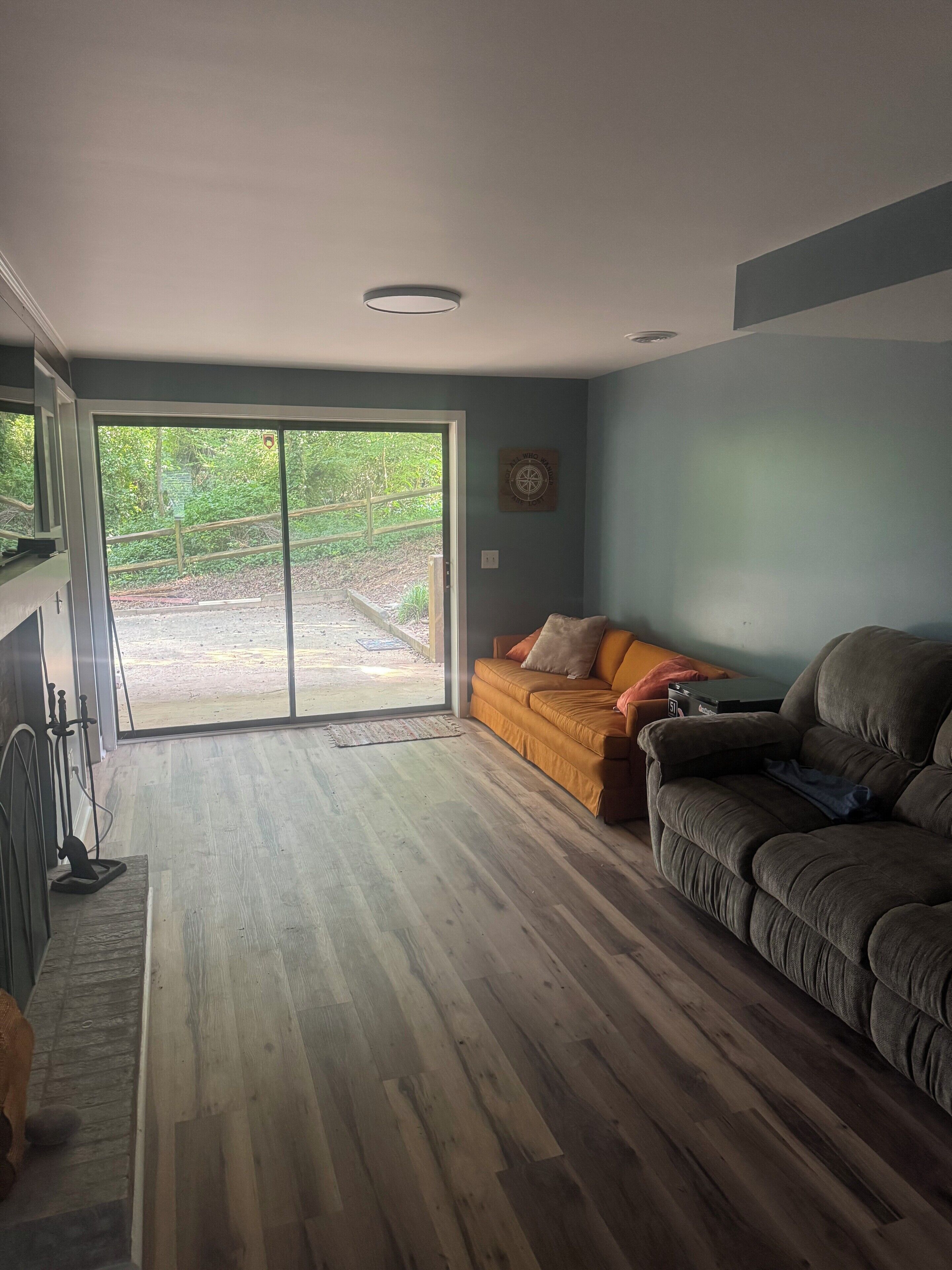 A living room with a wooden floor, a sofa, a couch, and a sliding glass door leading to a patio.
