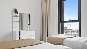 Une chambre d’hôtel avec deux lits, une commode blanche, un miroir et une grande fenêtre donnant sur la ville.