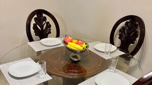 Una mesa de vidrio redonda con un frutero en el centro, rodeada de sillas con respaldos ornamentados.