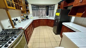 Una cocina con estufa a gas, horno, refrigerador, gabinetes de madera y una ventana con cortinas.
